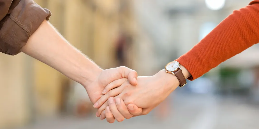 Duas pessoas de mãos dadas em uma rua, em um gesto de apoio e conexão.